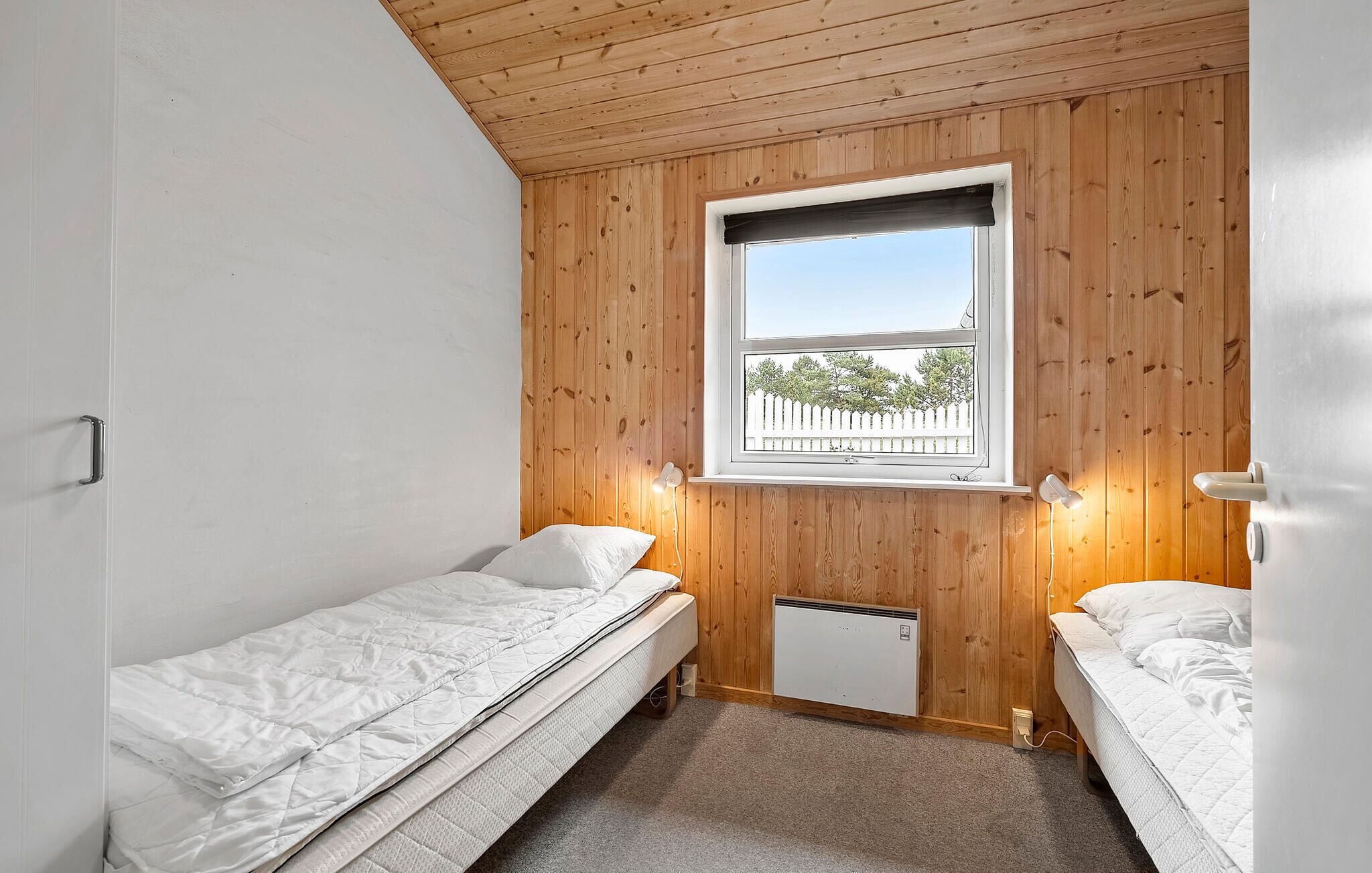 Un alojamiento pequeño y de una sola habitación con dos camas individuales, paredes de paneles de madera, una ventana con vistas y un pequeño calentador.