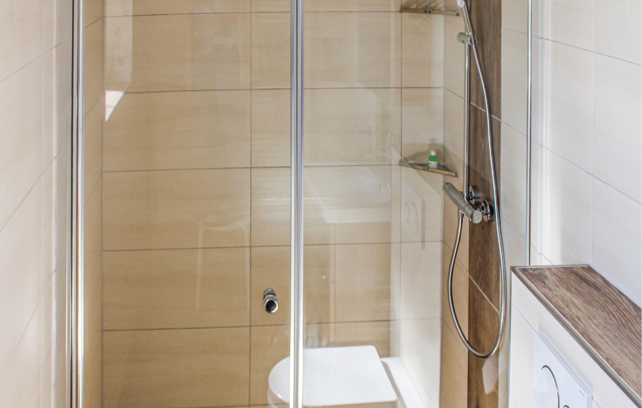 Een moderne badkamer met een douchecabine van glas, een wit toilet en een houten aanrecht.