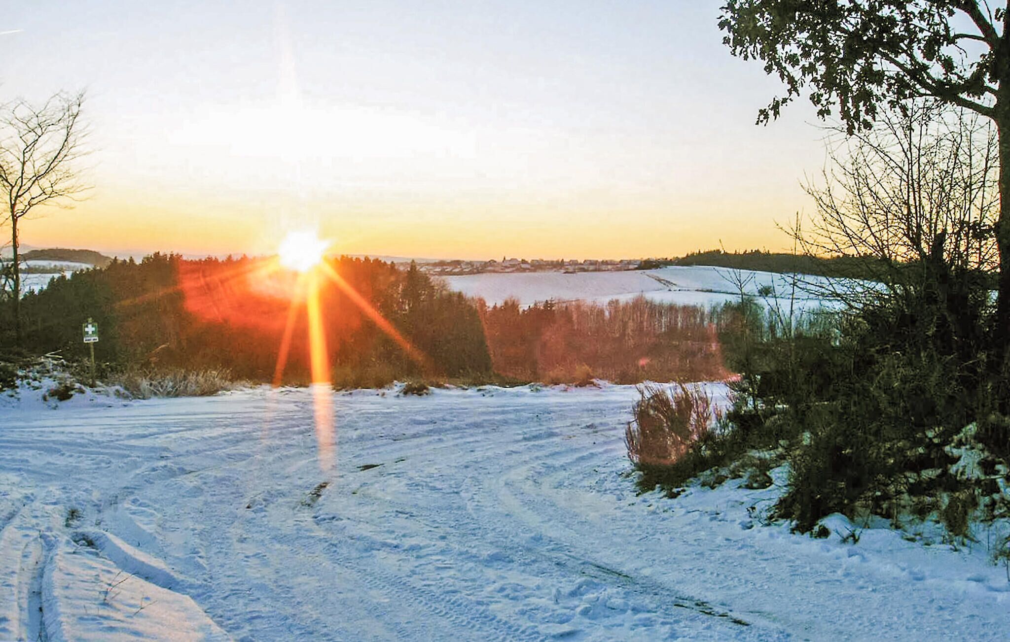 Eine verschneite Landschaft mit klarem Himmel und untergehender oder aufgehender Sonne.