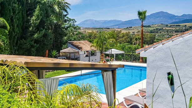 Piscina com vista para montanhas, uma estrutura com telhado de palha e vegetação exuberante.