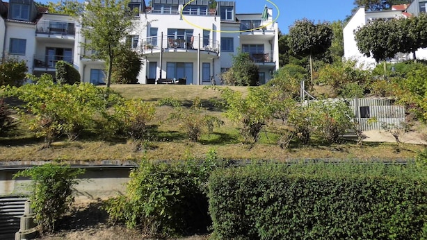 A multi-story residential building with balconies, a grassy slope, and a fence.