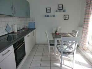 Une cuisine compacte avec des meubles blancs, un plan de travail noir et un coin repas comprenant des chaises et une table blanches.