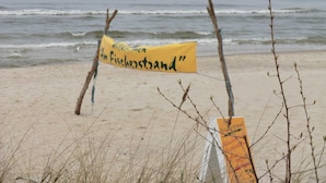 A beach with a yellow sign in the foreground and a body of water in the background.