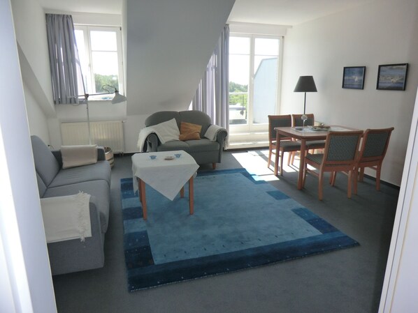 Un salon avec un canapé, une table et des chaises, une fenêtre avec des rideaux et une vue sur l’extérieur.
