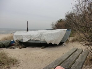 Ein Boot, bedeckt mit einer weißen Plane, am sandigen Strand. Eine hölzerne Bank steht in der Nähe.