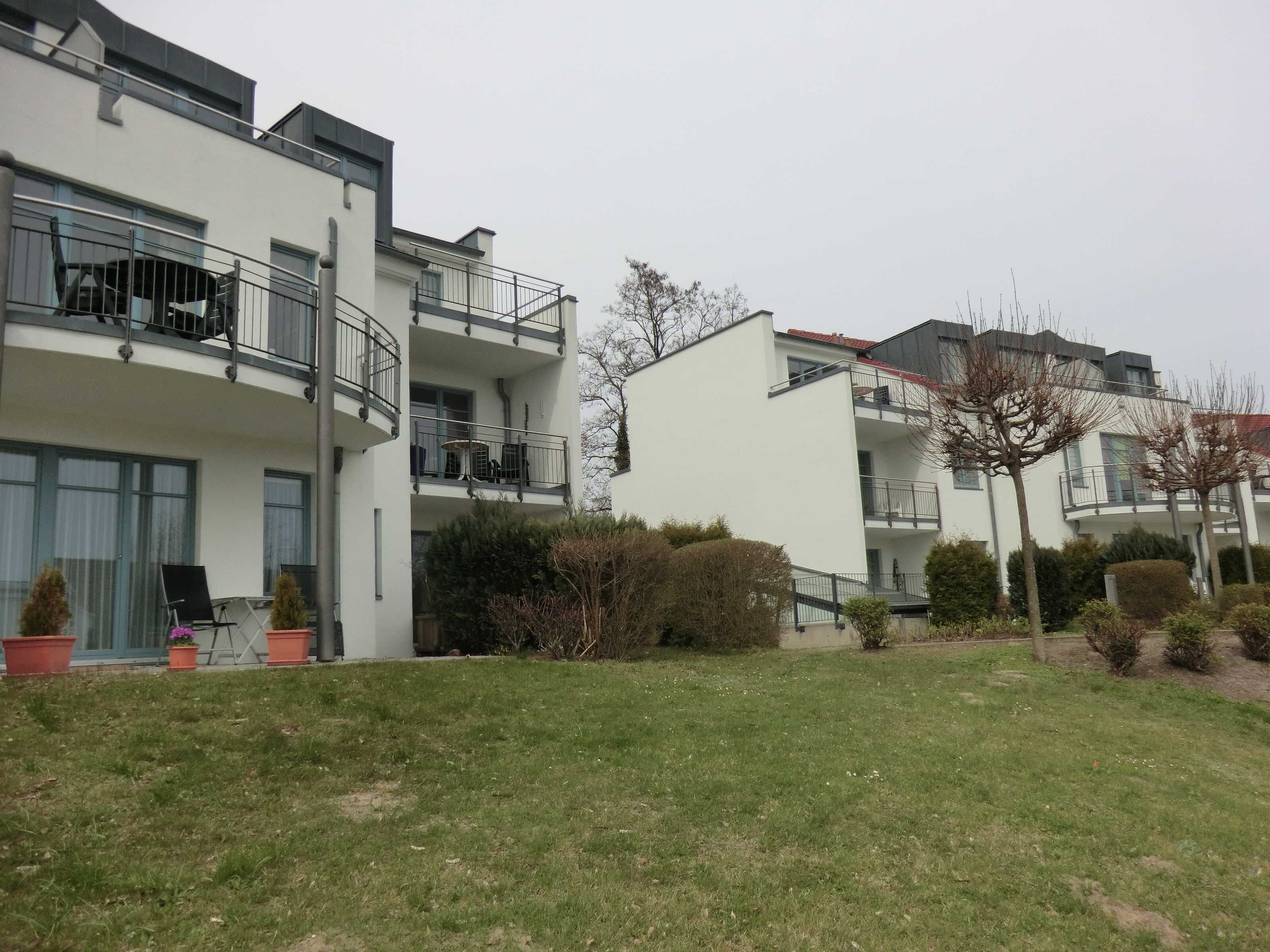 Ein modernes Mehrfamilienhaus mit Balkonen, einem begrünten Innenhof und Pflanzkübeln.