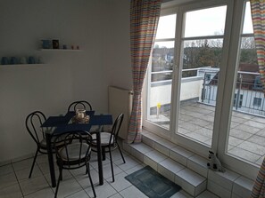A dining area with a table and chairs, a radiator, a window with curtains, and a view of the outside.