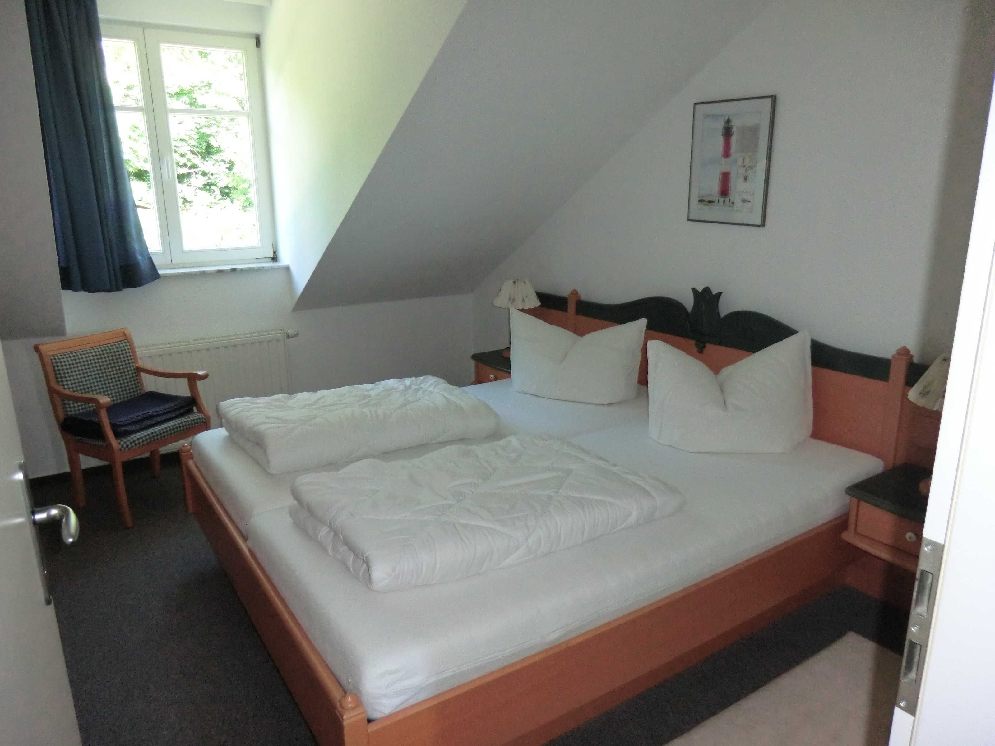 Ein Schlafzimmer mit einem Bett, einem Sessel, einem Nachttisch, einem Fenster und einem Bild an der Wand.