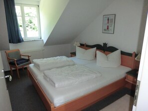 Una camera da letto con un letto, una sedia, un comodino, una finestra e un quadro appeso al muro.