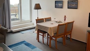A dining area with a table, chairs, a lamp, and two framed pictures on the wall.
