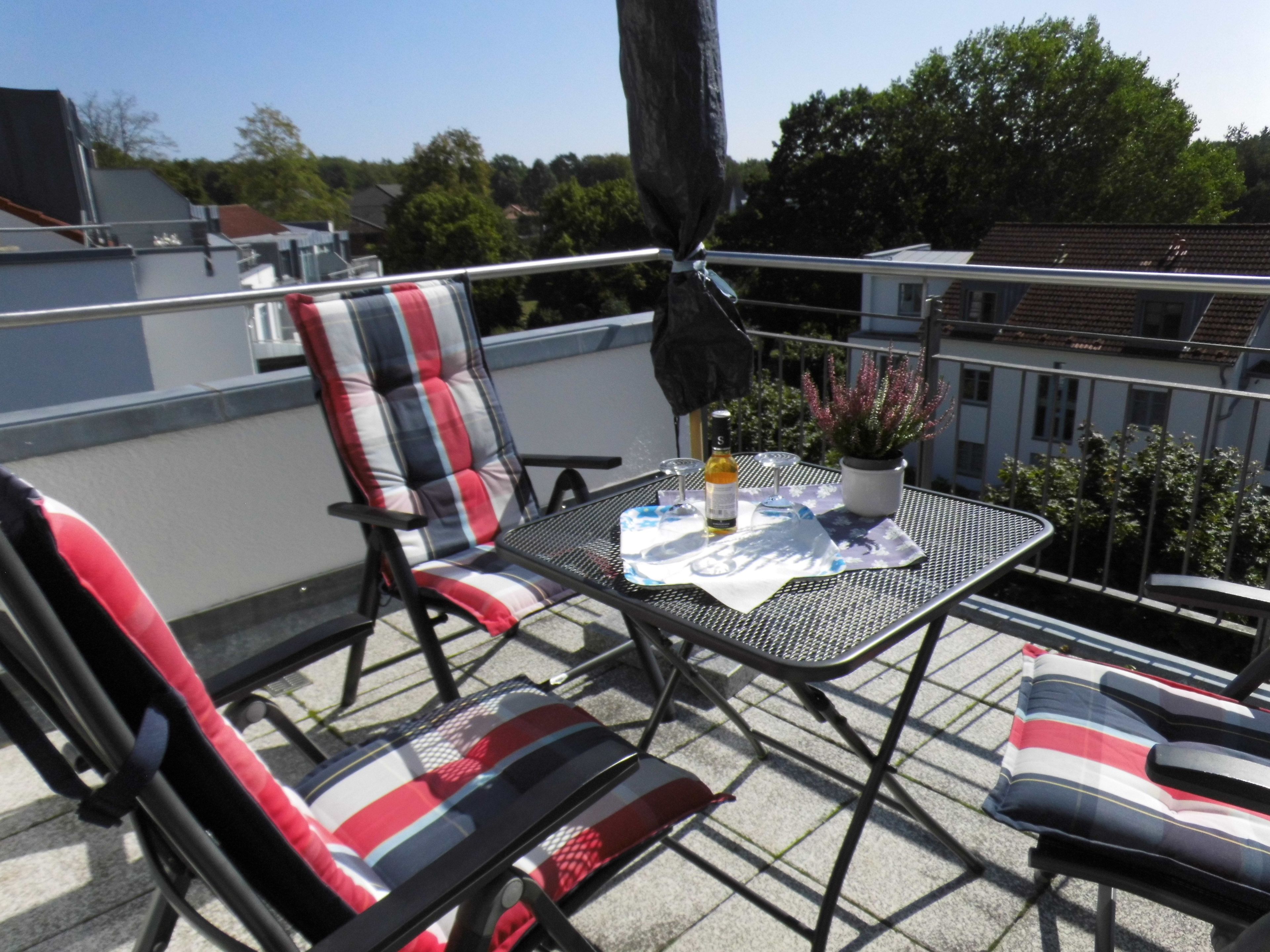 A balcony with a metal table, two chairs, a potted plant, and a bottle.