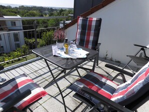 Un balcone con un tavolo in metallo, due sedie, una bottiglia di vino e una pianta in vaso.