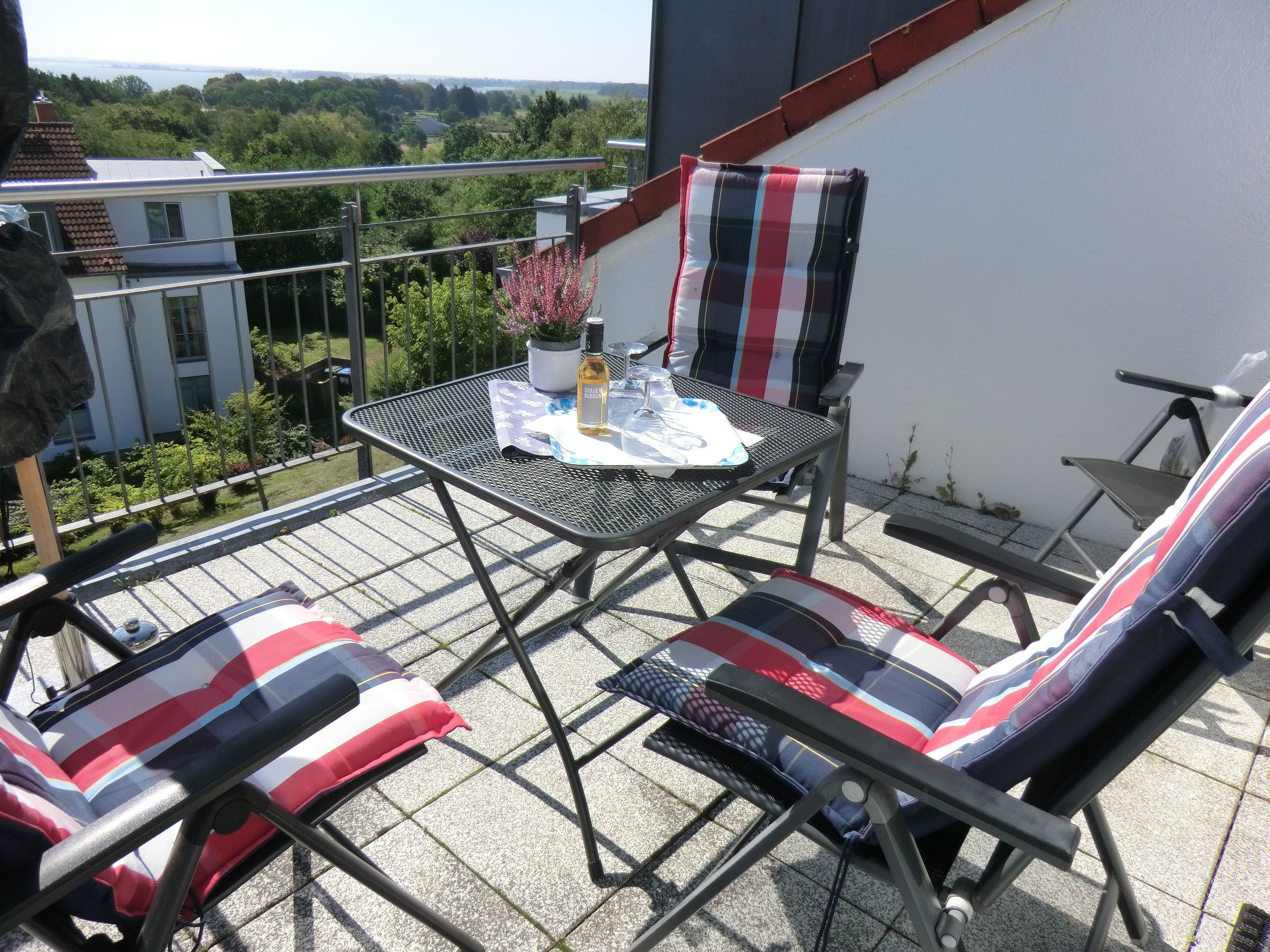 Un balcon avec une table en métal, deux chaises et un pot de fleurs.