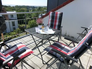 Un balcon avec une table en métal, deux chaises et un pot de fleurs.