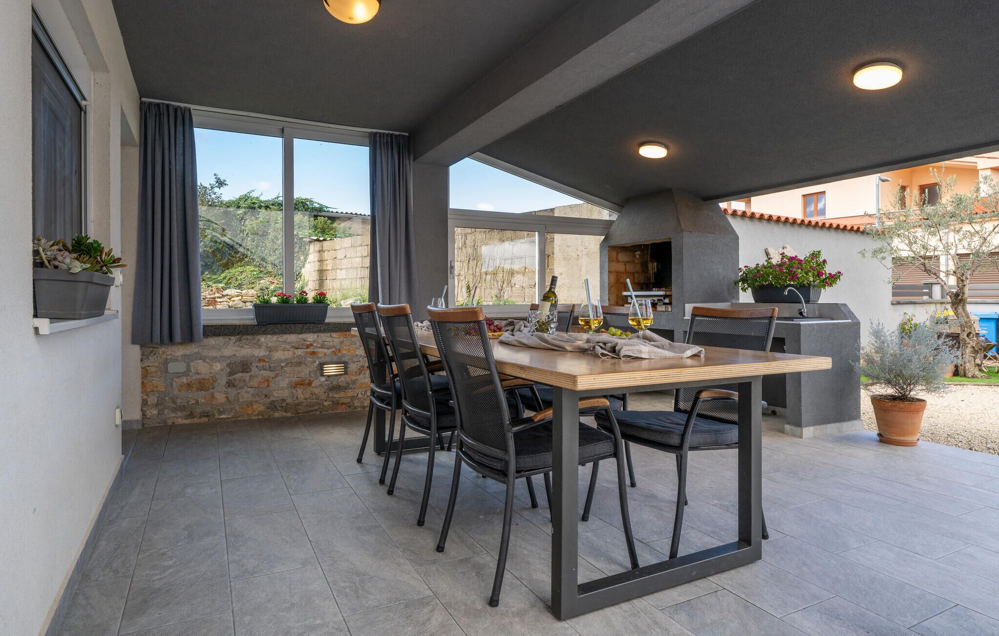 Un patio al aire libre con una mesa y sillas de madera, una parrilla y plantas en macetas.