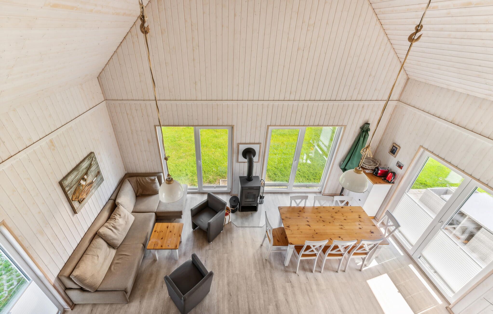 A cozy, well-lit room with a sofa, a dining table with chairs, a hanging light fixture, and a wood-burning stove.