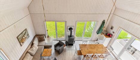 A cozy, well-lit room with a sofa, a dining table with chairs, a hanging light fixture, and a wood-burning stove.