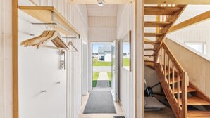 A narrow hallway with a wooden staircase on the right, a door at the end, and a view of a house outside.