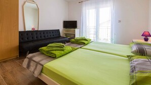 Quarto de hotel com duas camas, um sofá, uma televisão e uma janela com cortinas.