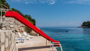 A red slide extending over a pool area with clear blue water and a stone wall.