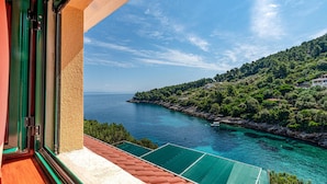 A balcony with a view of a coastal landscape, including a body of water and a hillside with vegetation.