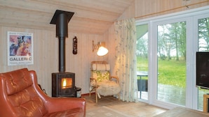 A cozy living room with a leather sofa, a wooden table, a fireplace, and a large window offering a view of the outdoors. - 3 bedroom cozy home in Oksbøl (Oksbøl)