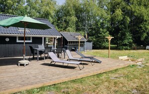 A deck with sun loungers and a table, a covered area with chairs, and a building with a metal roof.