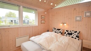 Un dormitorio con paneles de madera, una cama, un radiador, una ventana y dos lámparas fijadas a la pared.