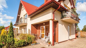 Une maison à deux étages avec un toit rouge, un balcon au deuxième étage et une façade en briques.