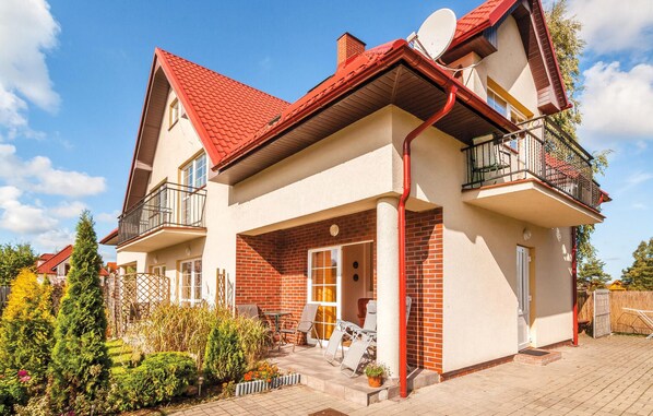 Une maison à deux étages avec un toit rouge, un balcon au deuxième étage et une façade en briques.