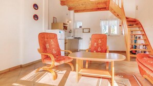 Une pièce chaleureuse avec un plafond en bois, une table à manger avec deux chaises, un coin cuisine équipé d’un réfrigérateur et un escalier menant à un autre niveau.