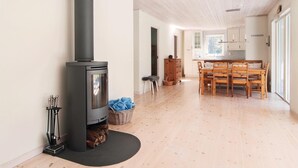 Un salón amplio con estufa de leña, una mesa de comedor con sillas y una cocina al fondo.