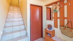 Una escalera que lleva a una puerta de madera, una cesta tejida en la pared y un estante de madera con un florero.