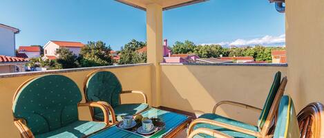 A balcony with wicker chairs and a table, overlooking a residential area with houses and trees.