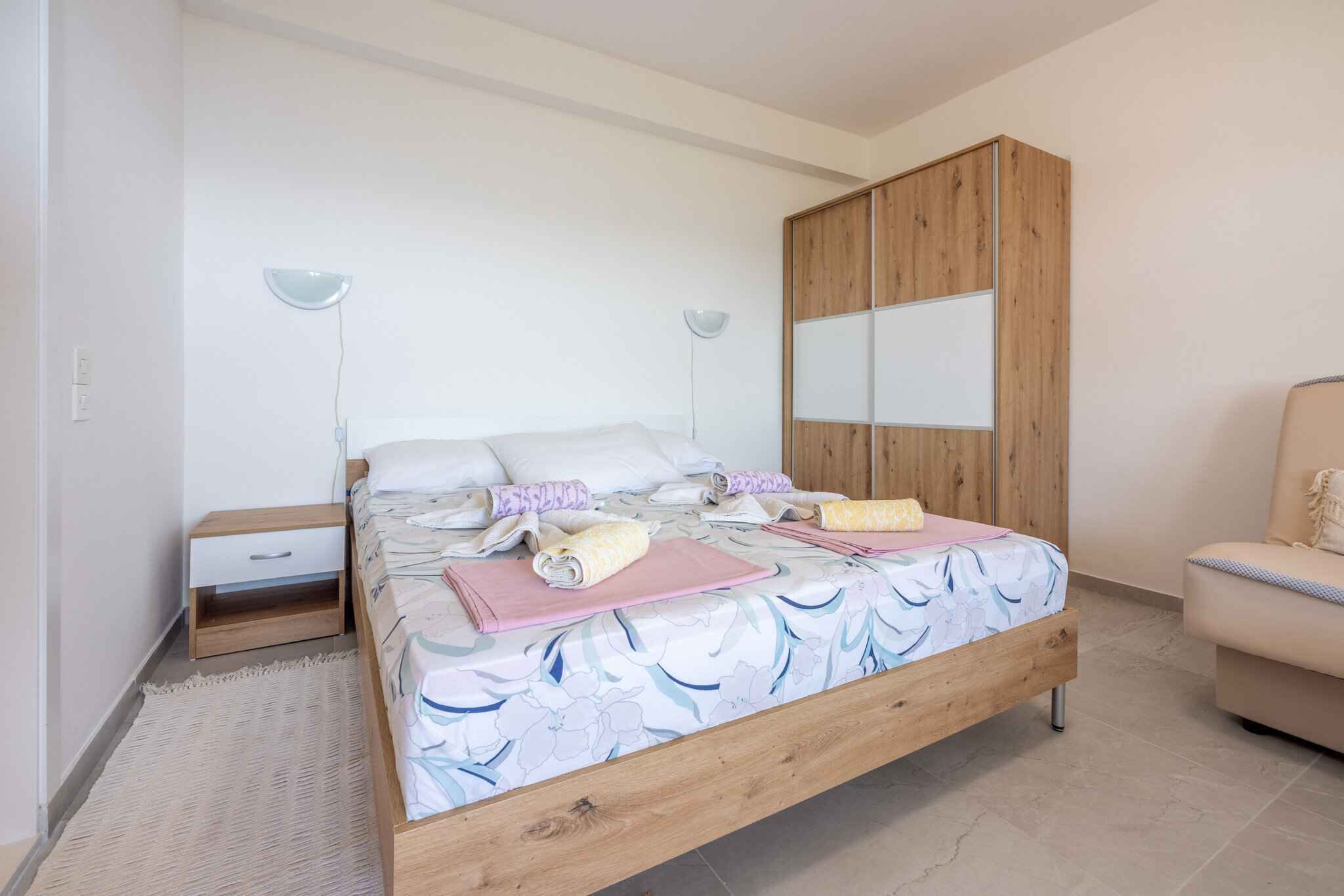 A bedroom with a wooden bed, a nightstand, a wardrobe, and a chair.