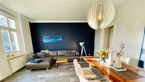 Een moderne woonkamer met een hoekbank, een houten eettafel en een groot raam.
