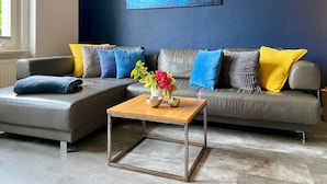Een moderne woonkamer met een grijze modulaire bank, een houten salontafel en een blauw abstract schilderij aan de muur.