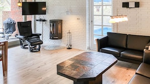 A modern living room with a wooden coffee table, black leather sofa, and a TV mounted on a brick wall. - Awesome home in Rømø with kitchen (Rømø)