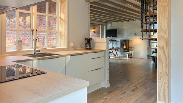 A modern kitchen with a large window, a built-in stove, and a wooden staircase leading to a loft area. - Awesome home in Rømø with kitchen (Rømø)