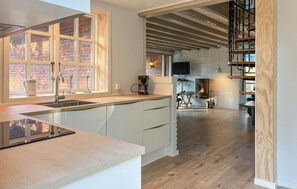 A modern kitchen with a large window, a built-in stove, and a wooden staircase leading to a loft area.