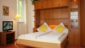 A double bed with white and yellow pillows, a wooden headboard, a television on a wooden stand, and a red polka dot carpet. - 2-room apartment no. 6, 35m², DG, West - Waldhaus Gronenberg (Scharbeutz)