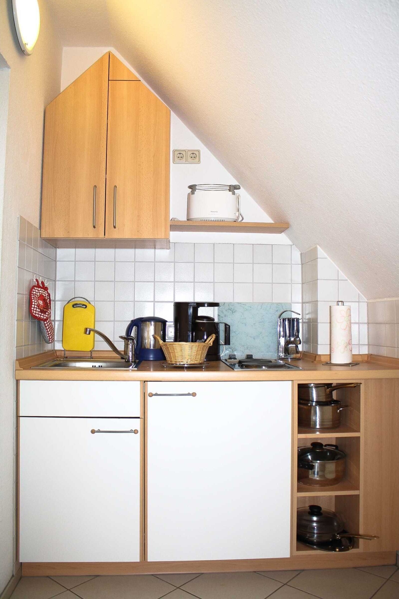 A compact kitchen with wooden cabinets, a sink, and various appliances including a kettle and a coffee maker.
