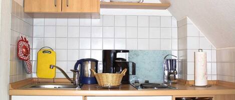 A compact kitchen with wooden cabinets, a sink, and various appliances including a kettle and a coffee maker.