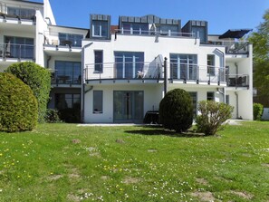 Un immeuble résidentiel à plusieurs étages, doté de balcons, d’une pelouse bien entretenue et surplombant un ciel dégagé.
