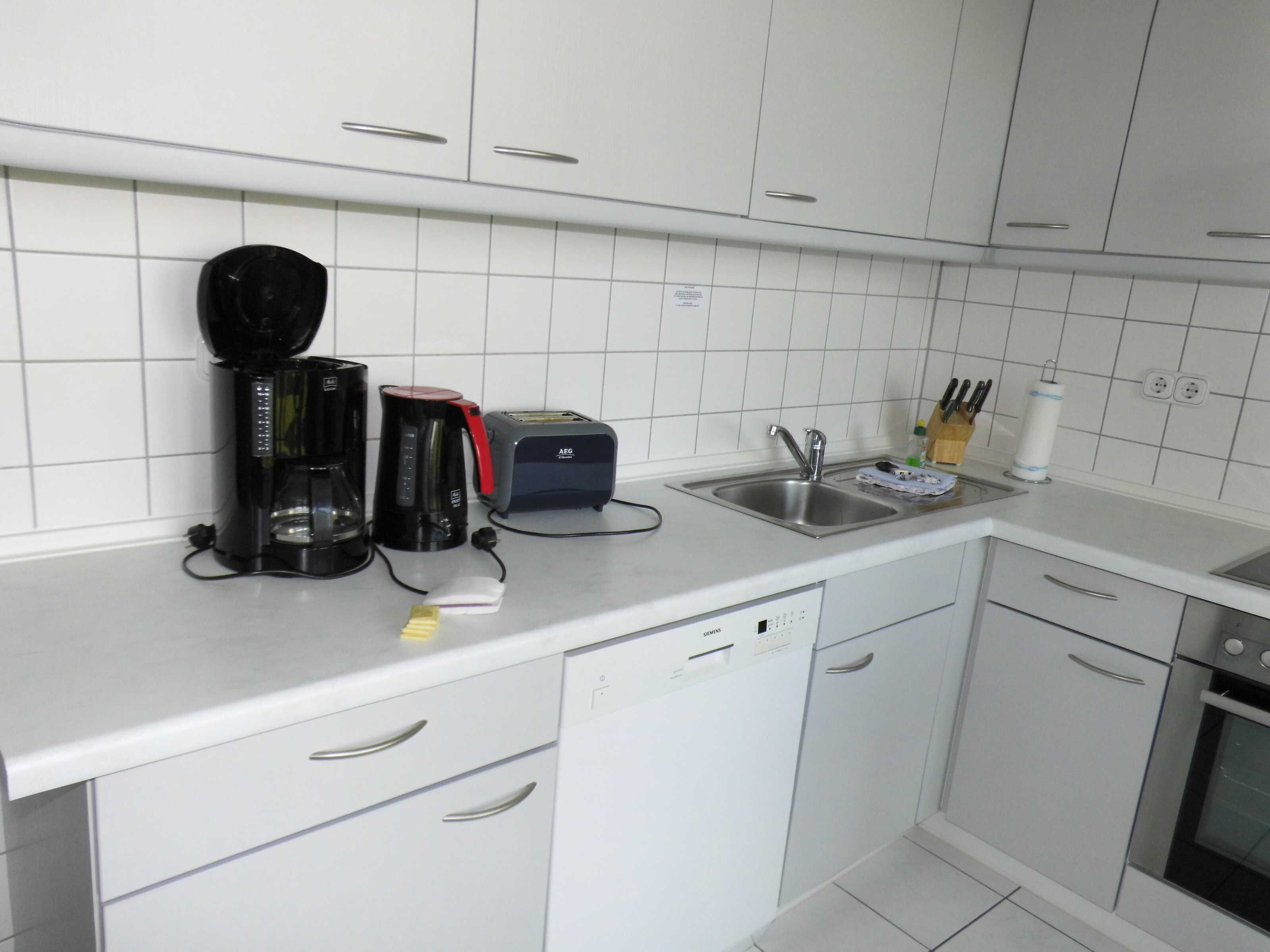 A kitchen with white cabinets, a coffee maker, a toaster, a sink, and a dishwasher.