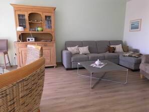 Un salon avec un canapé gris, un meuble en bois et un fauteuil en osier.