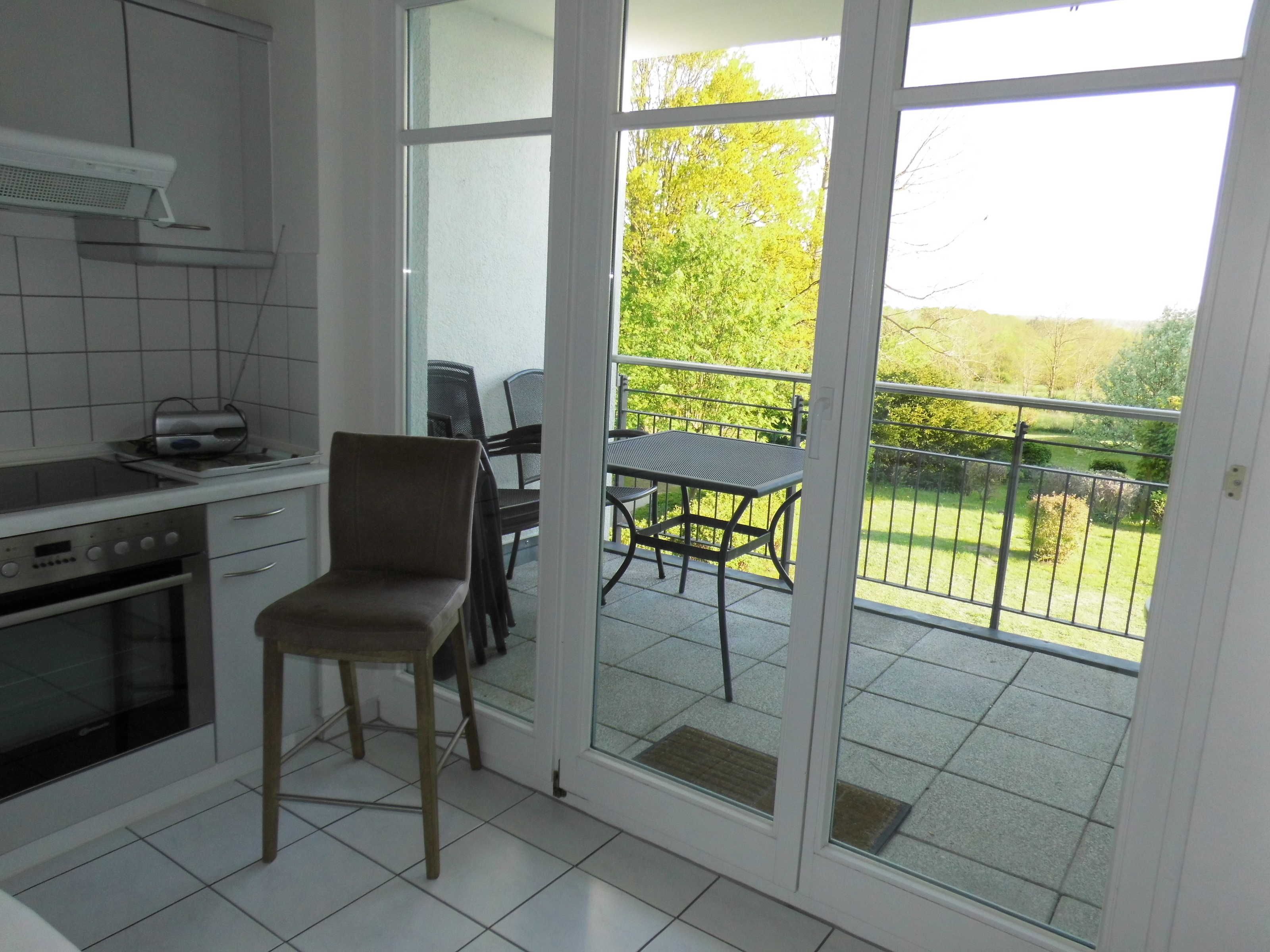 Une cuisine avec un coin repas, une table et des chaises, et une vue sur un paysage verdoyant par une porte vitrée.