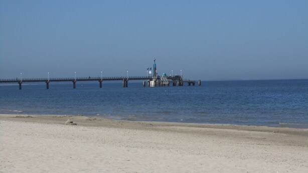 Eine Pier, die sich in ruhiges Wasser erstreckt, mit wolkenlosem Himmel.