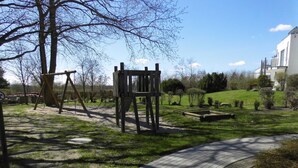 Ein Park mit einem Spielplatz, einem gepflasterten Weg und einem Gebäude im Hintergrund.