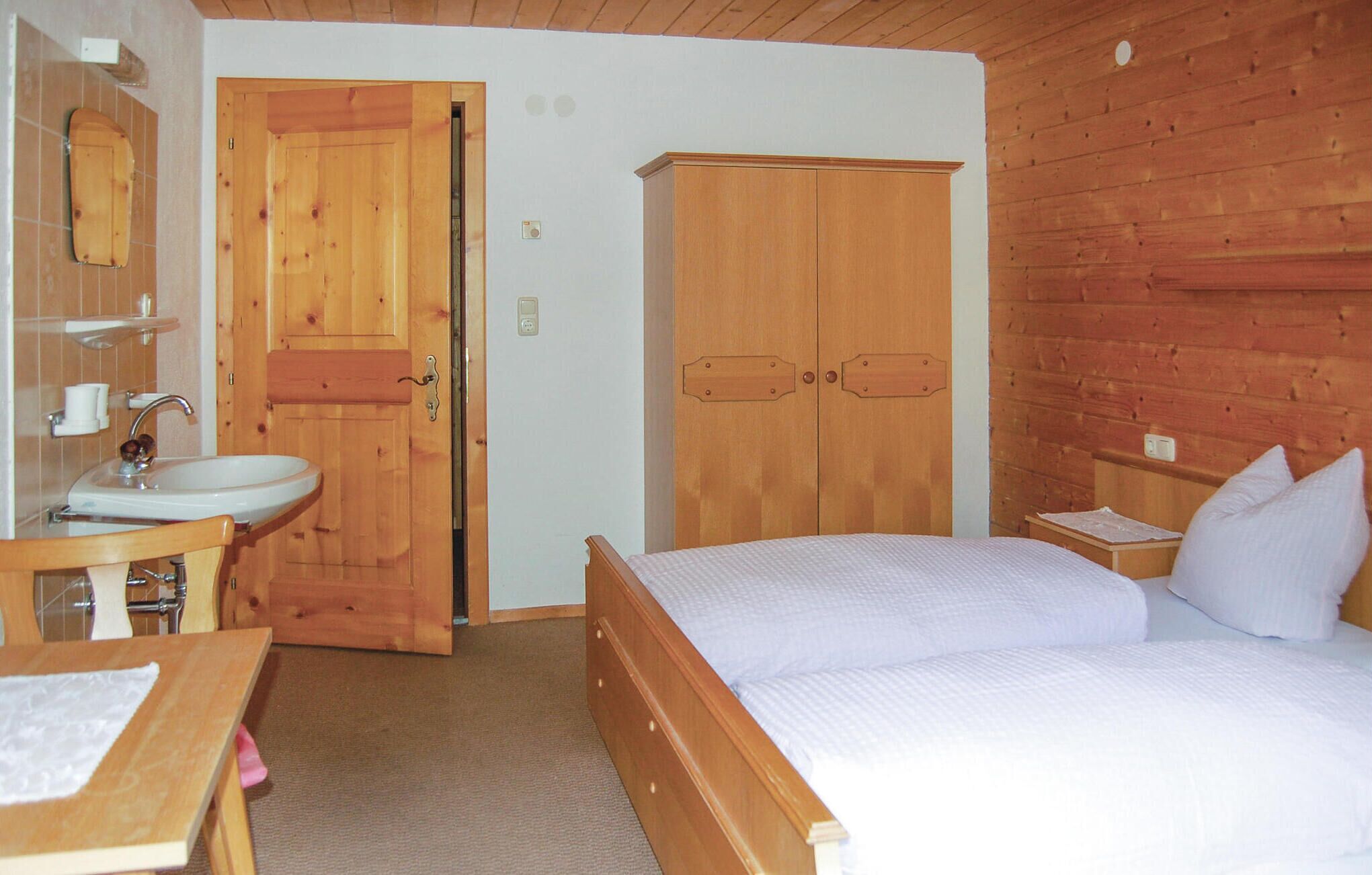 Ein Zimmer aus Holz mit einem Bett, einem Holzschrank, einem Waschbecken und einem Spiegel.